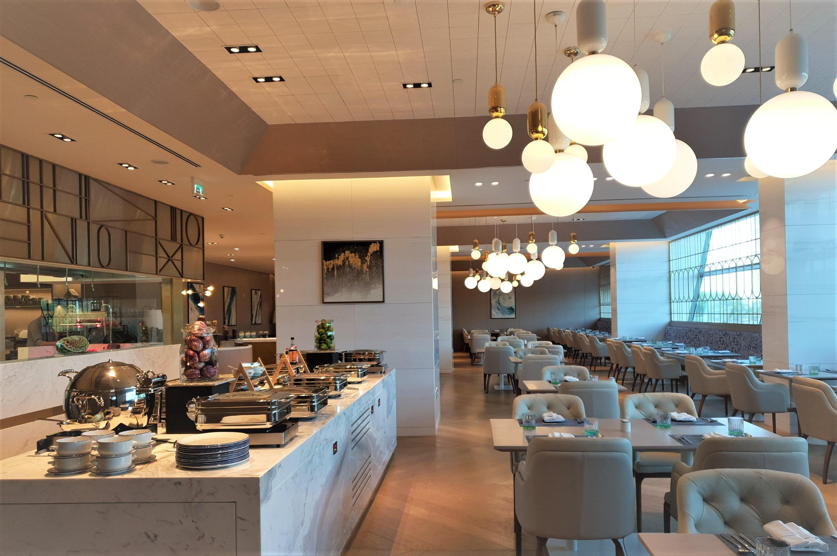 Steigenberger Hotel Doha Eksteriør billede The photo shows the interior of a modern restaurant. It features a well-organized buffet area with various dishes displayed on a marble counter. Elegant dining tables and chairs are set up throughout the space, creating a comfortable atmosphere. The 